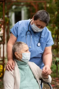 Healthcare worker comforting an elderly patient outdoors, both wearing face masks, symbolizing care and safety in a medical setting
